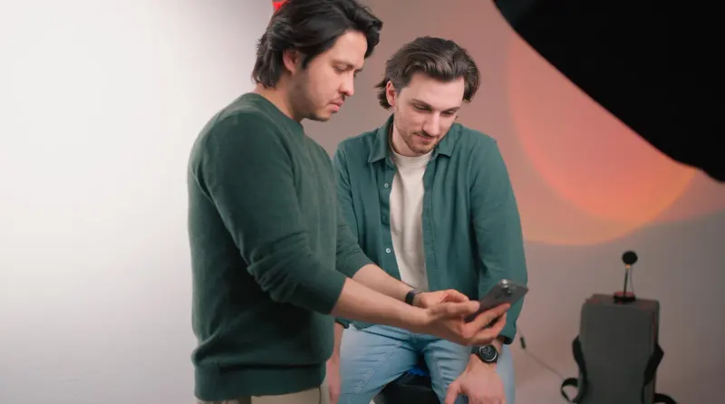 Two Steepe & Co project team members looking at a phone together in a studio with warm orange lighting