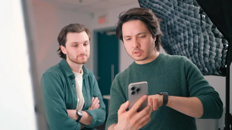 Two Setsail video team members on set checking footage on a phone beside a studio softbox light