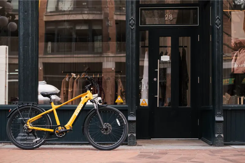 Yellow ENVO e-bike parked on a brick sidewalk outside a black storefront with clothing in the window