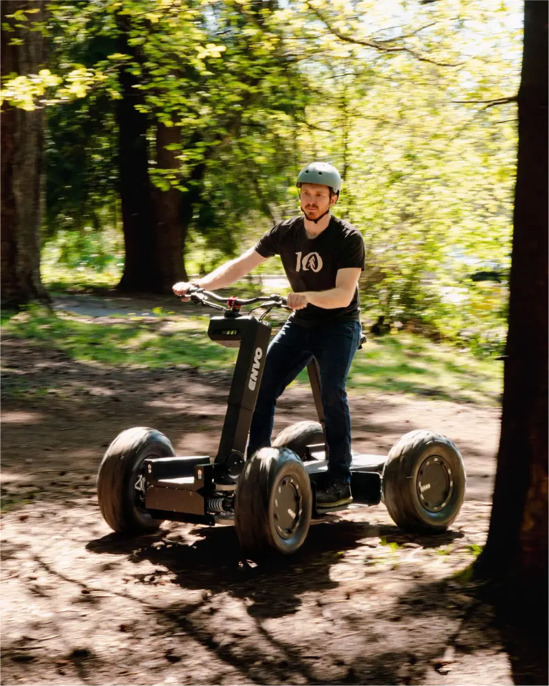 Rider with a helmet standing on a black four-wheeled ENVO vehicle on a sunlit forest trail