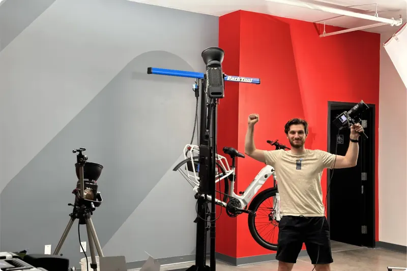 A man cheering beside an e-bike in a repair stand, in front of a red wall
