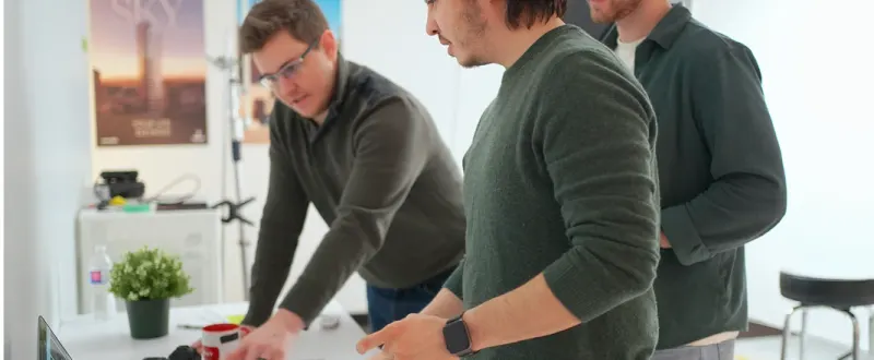Three Setsail Marketing team members looking over a laptop at a desk in the studio