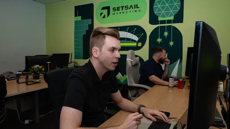 A Setsail developer at his monitor in the office, the Setsail mural on the wall behind.