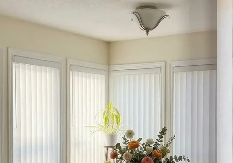 White vertical blinds across a bay of breakfast-nook windows, from Ray Blinds’ ad creative