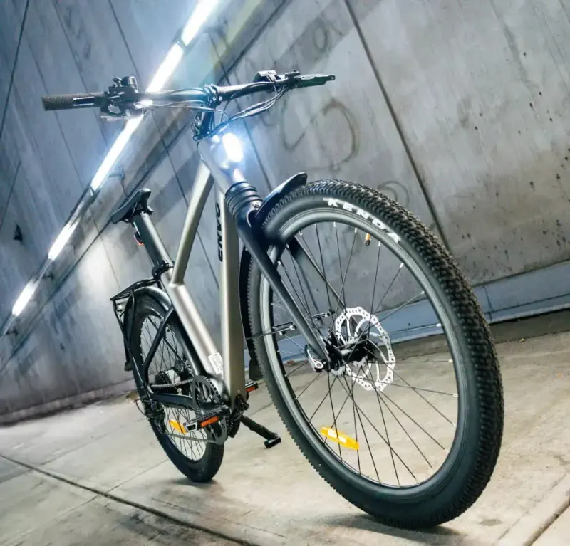 A silver Envo e-bike with its headlight on, shot low in a concrete tunnel